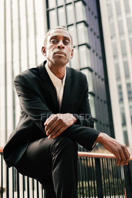 Selbstbewusster schwarzer Geschäftsmann stützt sich auf Geländer — Stockfoto