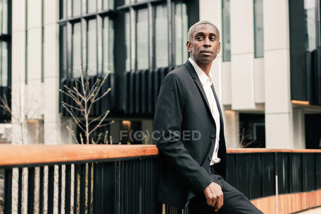 Fiducioso uomo d'affari nero appoggiato alla ringhiera — Foto stock