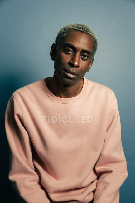 Adult African American male model in trendy pink sweatshirt looking at camera against blue background — Stock Photo
