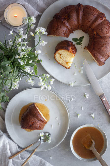 Top view of delicious Bundt cake with apple sauce placed on table near white flowers and burning candle — Stock Photo