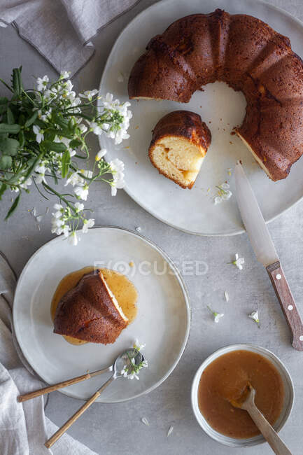 Top view of delicious Bundt cake with apple sauce placed on table near white flowers and burning candle — Stock Photo