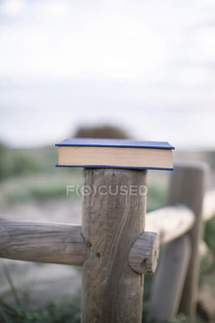 Dall'alto libro chiuso con copertina blu posto su recinzione in legno nella giornata di sole con spiaggia sullo sfondo — Foto stock