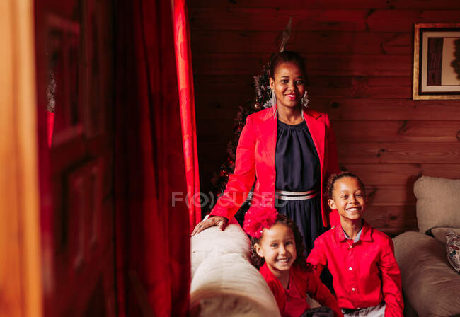 Jovem alegre preto fêmea com bonito rindo irmãos em roupas vermelhas olhando para a câmera enquanto passar o tempo juntos em casa de campo acolhedor — Fotografia de Stock