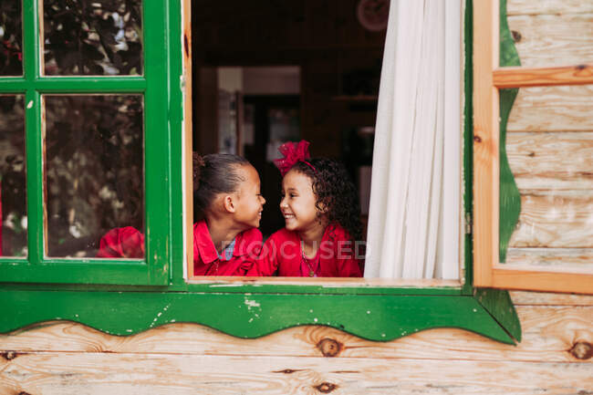 Simpatici fratellini neri sorridenti attraverso la finestra aperta della cabina in legno — Foto stock