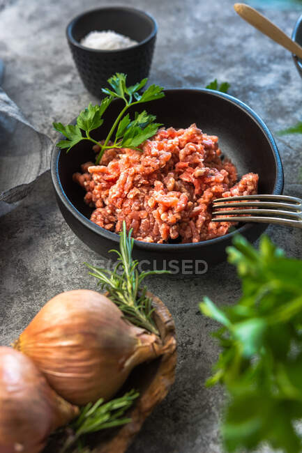 D'en haut vue oignons crus et herbes placées sur la table grise près du bol avec du sel de viande hachée dans la cuisine — Photo de stock