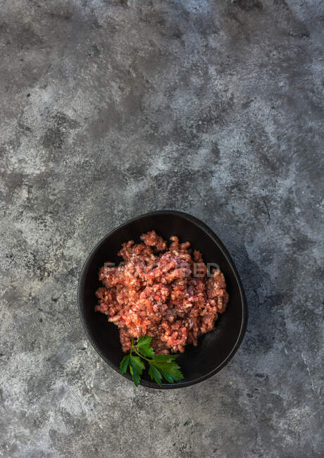 Da sopra vista dall'alto erbe su ciotola con carne macinata disposta su tavolo grigio in cucina — Foto stock