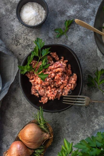De cima vista superior cebolas cruas e ervas colocadas na mesa cinza perto da tigela com sal de carne picada na cozinha — Fotografia de Stock