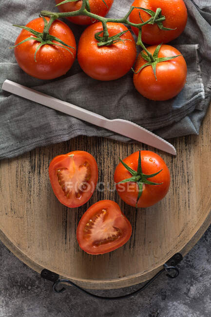 Halved and whole fresh tomatoes placed wooden board on rough gray table during food preparation in kitchen — Stock Photo