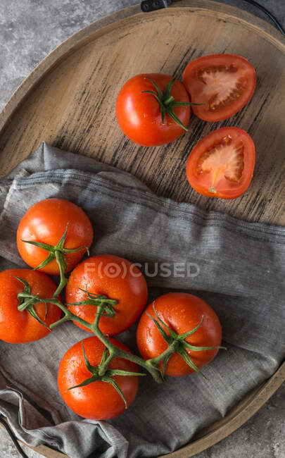 Tomates frescos enteros y cortados a la mitad colocados sobre una mesa gris rugosa durante la preparación de alimentos en la cocina - foto de stock