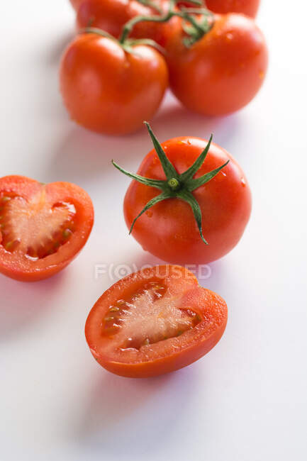Vista superior de racimo de tomates maduros naturales enteros y cortados a la mitad colocados sobre fondo blanco - foto de stock