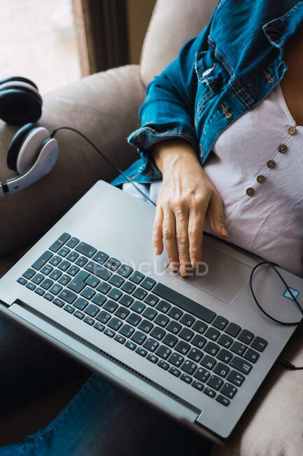 Зверху анонімна жінка сидить у кріслі біля навушників і ноутбука під час роботи над віддаленим проектом вдома. — стокове фото