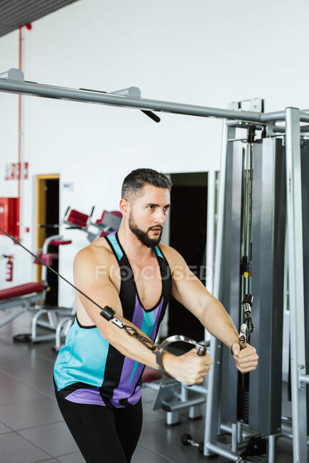 Potente culturista masculino en ropa deportiva realizando ejercicio con máquina de cable durante un intenso entrenamiento en gimnasio contemporáneo con equipos modernos - foto de stock