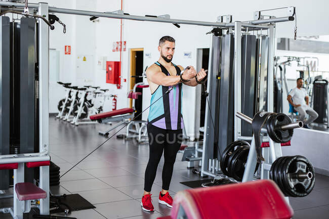 Potente culturista masculino en ropa deportiva realizando ejercicio con máquina de cable durante un intenso entrenamiento en gimnasio contemporáneo con equipos modernos - foto de stock