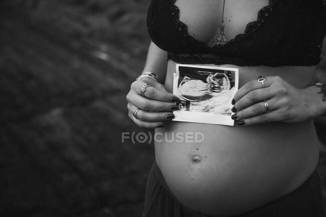 Tatuato elegante donna incinta in reggiseno con immagine a sonogramma sulla pancia in piedi su maestosa costa — Foto stock