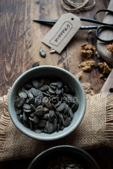 Vista superior da tigela de sementes de abóbora preta colocadas em guardanapo de linho perto de tesoura retro e etiqueta de granola — Fotografia de Stock