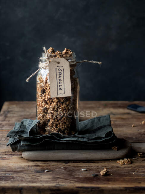 Vaso di vetro di miglio naturale e granola di quinoa con etichetta posta su tovagliolo su tavolo rustico — Foto stock