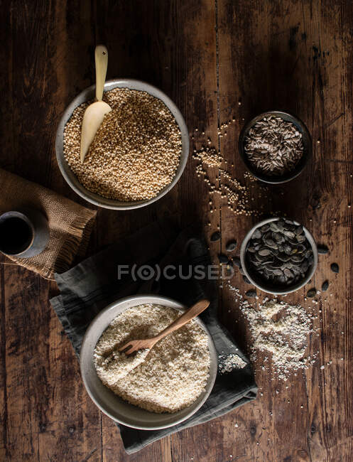 Vue du dessus des bols avec mil et quinoa pour la préparation de granola placés sur une table en bois près des serviettes et des graines — Photo de stock