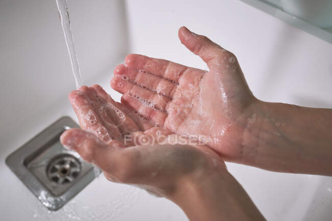 Зверху ми бачимо незбагненного хлопчика, який миє руки під водою в сучасній ванній кімнаті. — стокове фото