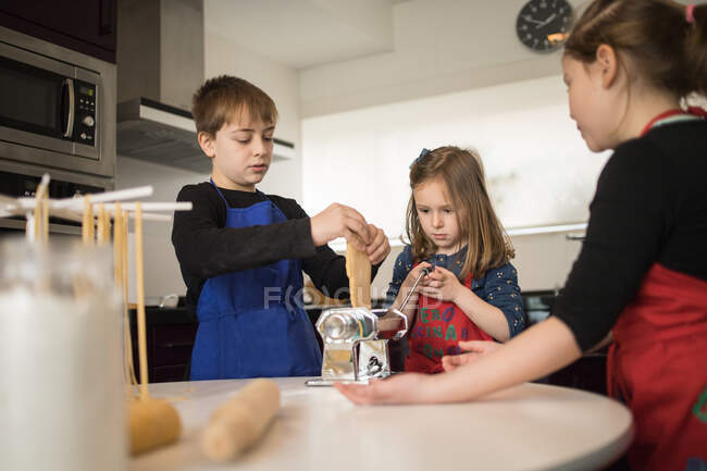 Family using pasta machine while preparing homemade noodles in home kitchen — Stock Photo