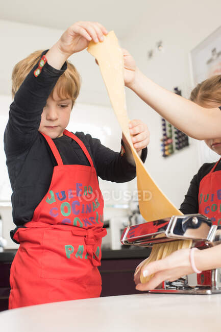 Маленька дівчинка з братом використовує макаронні машини, готуючи домашню локшину на домашній кухні — стокове фото