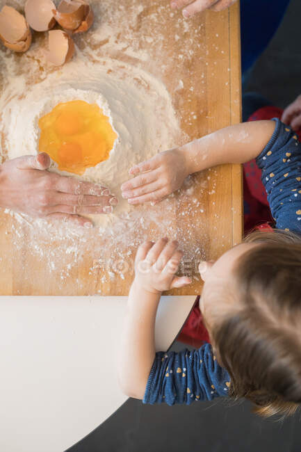 Дети готовят тесто стоя вместе за кухонным столом с мукой — стоковое фото