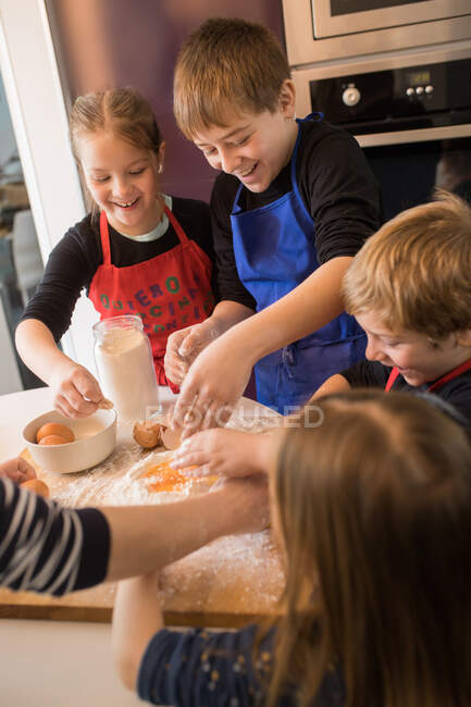 Діти готують тісто, стоячи разом за кухонним столом з борошном — стокове фото