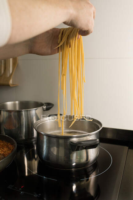 Erntehelfer legt frische hausgemachte Nudeln in einen Metalltopf mit kochendem Wasser, während er das Abendessen in der Küche zubereitet — Stockfoto