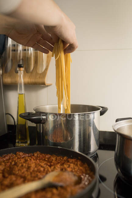 Erntehelfer legt frische hausgemachte Nudeln in einen Metalltopf mit kochendem Wasser, während er das Abendessen in der Küche zubereitet — Stockfoto