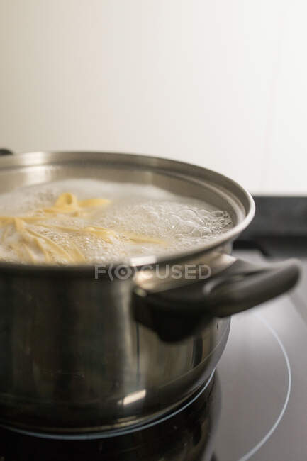 Крупним планом металева каструля з киплячою водою і домашньою макаронами, розміщеними на плиті на кухні — стокове фото