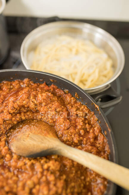 From above closeup of pan with traditional bolognese sauce placed on kitchen table near pot with cooked pasta — Stock Photo