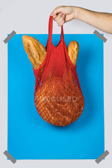 Unbekannter trägt roten Netzsack mit frischen Brotlaiben gegen blaues Rechteck beim Zero Waste Shopping — Stockfoto