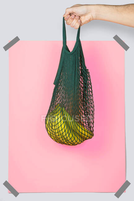 Personne méconnaissable portant un sac filet avec des bananes mûres contre le rectangle rose lors du shopping zéro déchet — Photo de stock