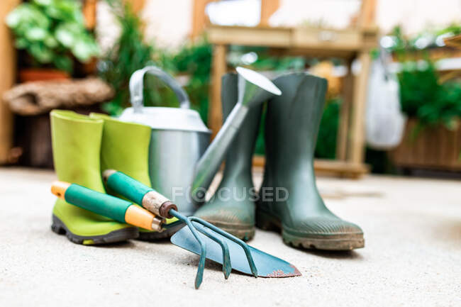 Gardening tools placed on floor near rubber boots and watering can in greenhouse — Stock Photo