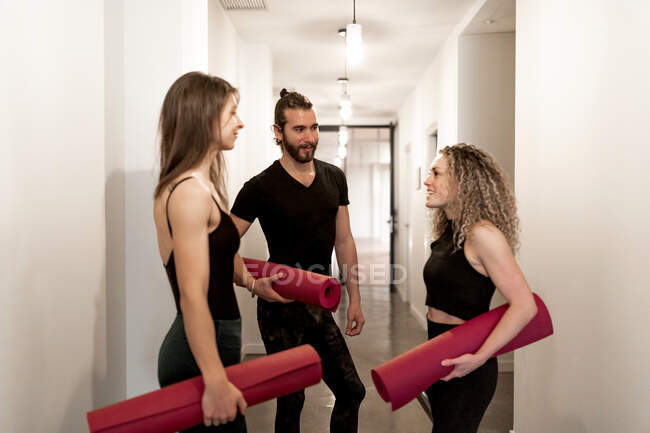 Young man and women with mats speaking with each other while standing in studio corridor during yoga training — Stock Photo