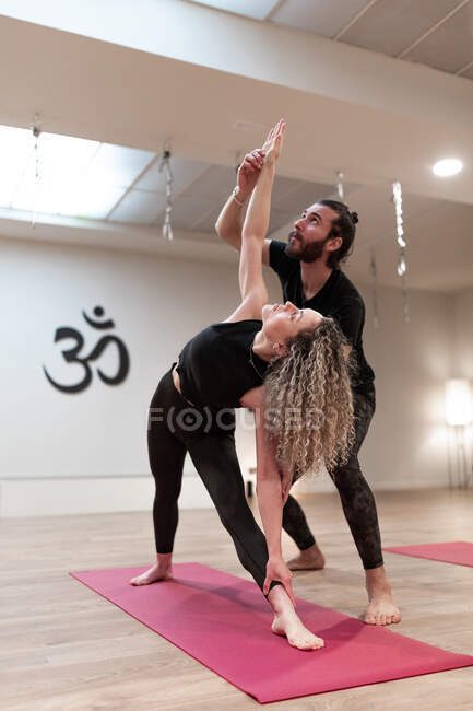 Сбалансированная спокойная женщина и мужчина учитель помогает корректировать позу на расширенный угол позы на йоге класса — стоковое фото