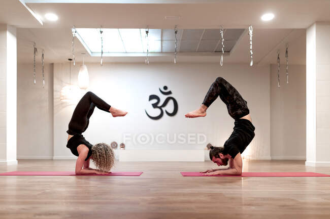 Side view of young man and woman in sportswear bending back while doing yoga exercise during training in spacious studio — Stock Photo