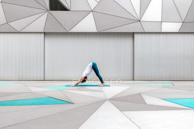 Side view of adult male in sportswear doing Downward Facing Dog exercise while doing yoga against geometric wall in spacious room — Stock Photo