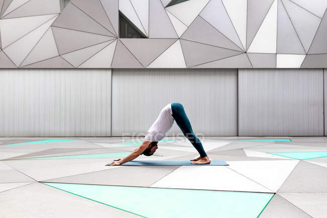 Seitenansicht eines erwachsenen Männchens in Sportbekleidung, das im geräumigen Raum beim Yoga gegen eine geometrische Wand hetzt — Stockfoto