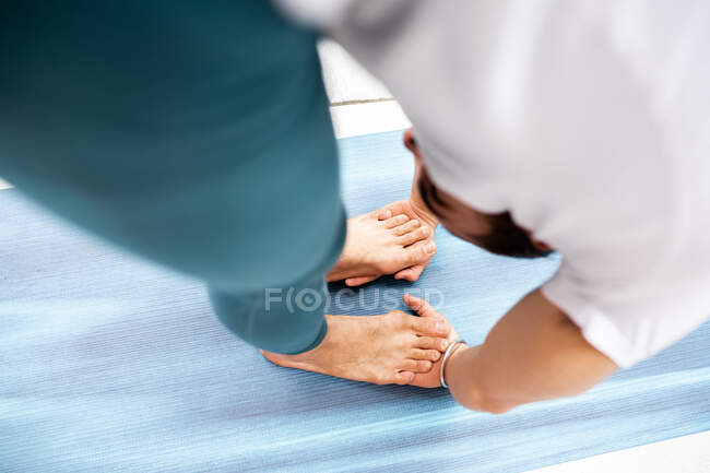 Зверху босоніж хлопець нахиляється вперед і наступає на руки, роблячи йогу на синьому килимку під час тренування йоги — стокове фото