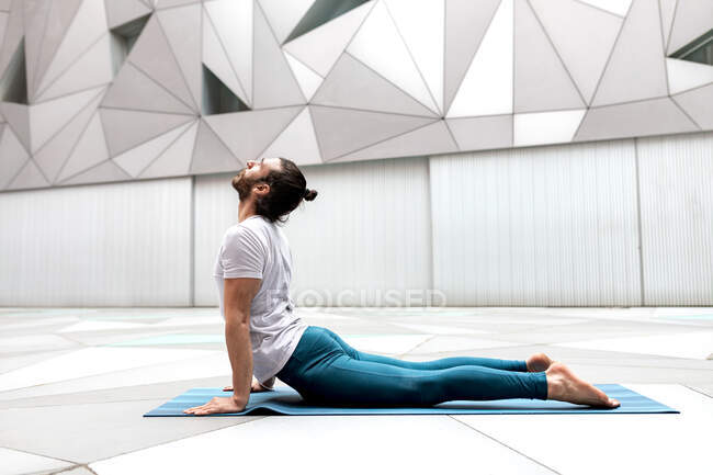 Side view of flexible barefoot male in sportswear doing Upward Facing Dog exercise in spacious room with geometric walls and floor — Stock Photo