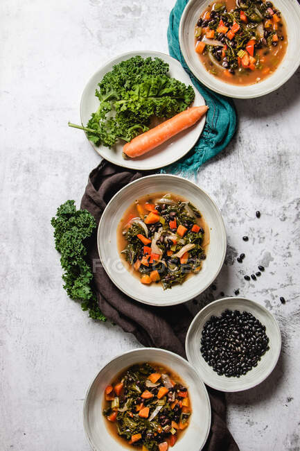 Top view of bowls with yummy kale soup with carrot and black seeds placed on gray table near napkins — Stock Photo