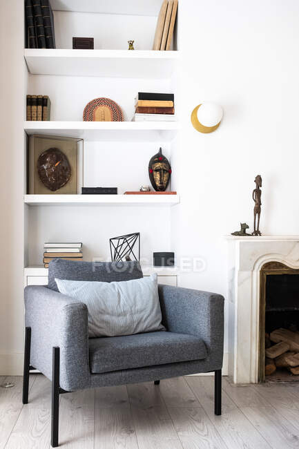 Comfortable grey seats located near fireplace and bookshelf in cozy living room in stylish apartment — Stock Photo
