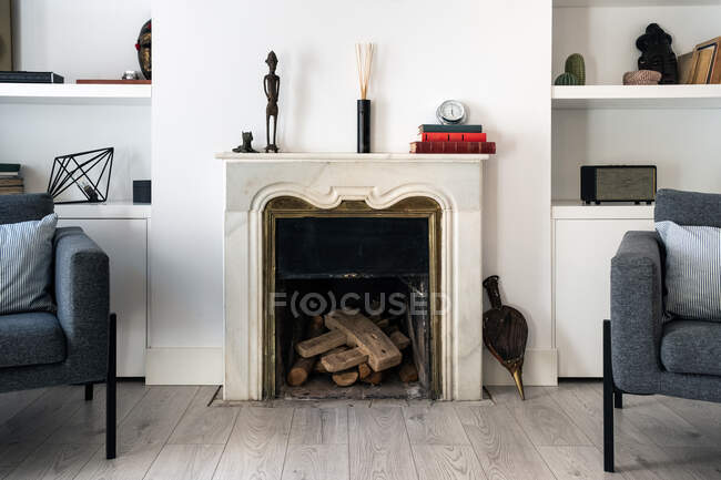 Comfortable grey seats located near fireplace and bookshelf in cozy living room in stylish apartment — Stock Photo