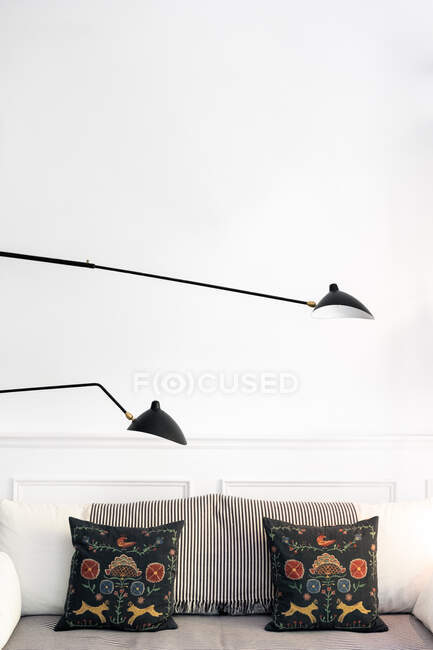 Sofá confortável com almofadas macias localizadas sob lâmpada de metal moderna na elegante e acolhedora sala de estar em casa — Fotografia de Stock