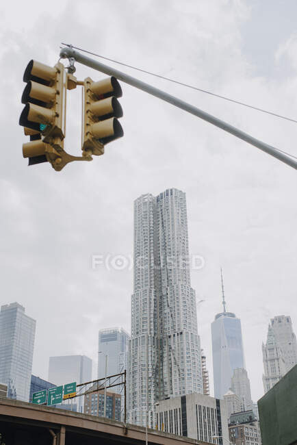 From below of traffic light hanging over road in New York City with contemporary skyscrapers and cloudy sky in background — Stock Photo