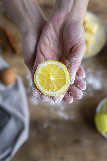 Зверху рука невизначеної жінки, вкрита борошном, тримає і показує на камеру свіжий напіврізаний лимон — стокове фото