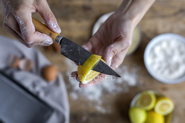 Зверху врожайна рука невизначеної жінки, покрита борошном очищає лимон і показує на камеру свіжий напіврізаний лимон з ножем — стокове фото