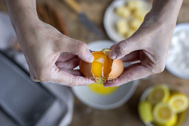 De cima vista superior fêmea irreconhecível quebrando ovo de galinha fresco em tigela enquanto cozinha pastelaria em uma mesa de madeira com ingredientes frescos — Fotografia de Stock