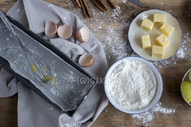 Вид зверху інгредієнтів рецепта торта, включаючи миску з борошном та яйцем, поміщені на забруднений дерев'яний стіл — стокове фото