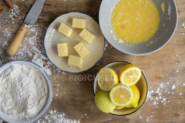 Vista superior de los ingredientes para la receta de la torta, incluyendo un tazón con harina y huevo colocado en una mesa de madera espolvoreada - foto de stock